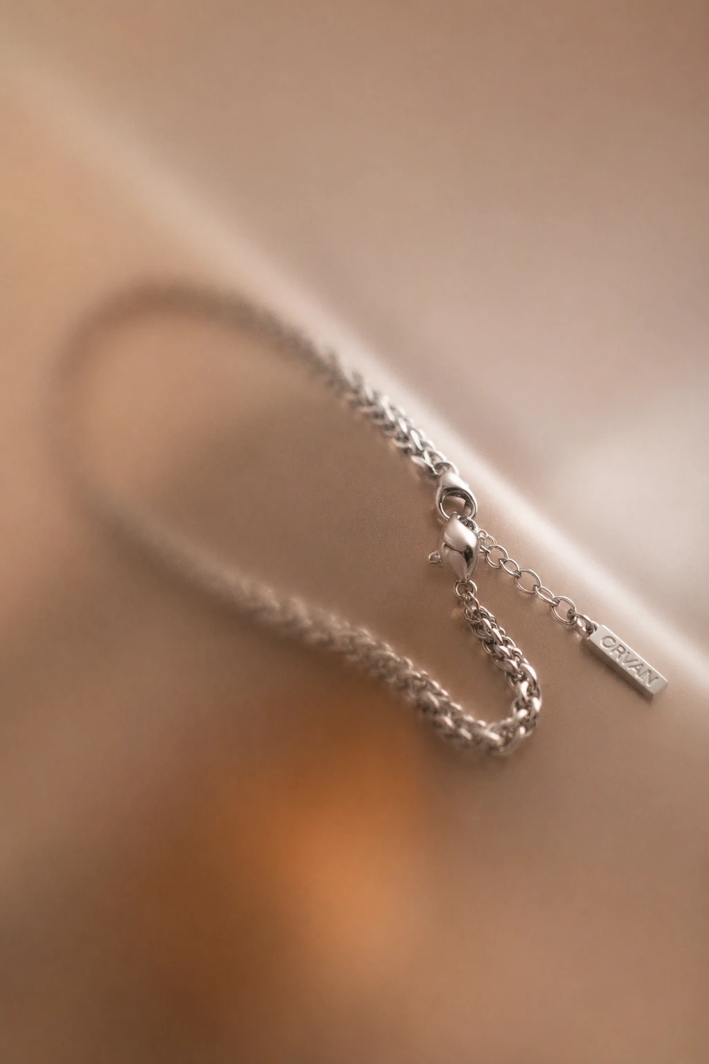 Ein ORVAIN Armband auf hellem Satin, Verschluss und Plakette im Licht