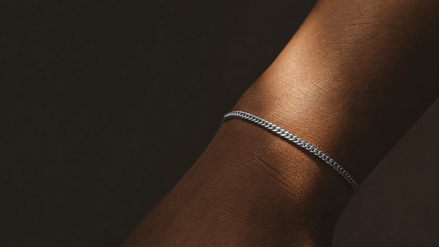Ein feines Panzerarmband am Handgelenk, warmes Seitenlicht