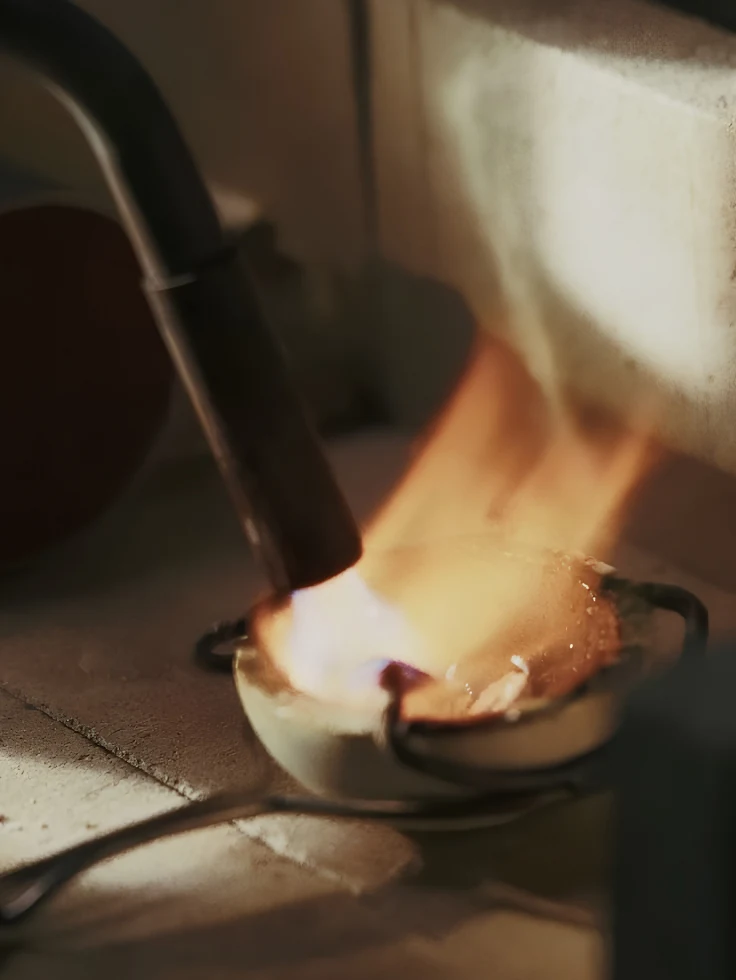 Eine Lötflamme über einer Schale, warmes Licht im Dunkeln